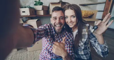 A couple happily holding the keys to a newly purchased home among moving boxes, shortly after completion